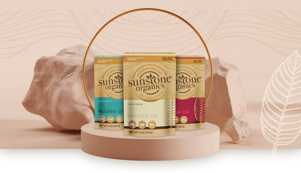 Three Sunstone Organics kratom packages, white, red and green vein, on a display stand